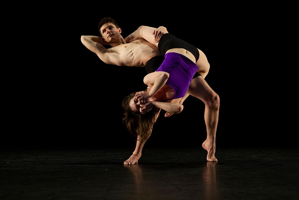 Two Kennesaw State University dance students perform on a darkened stage.