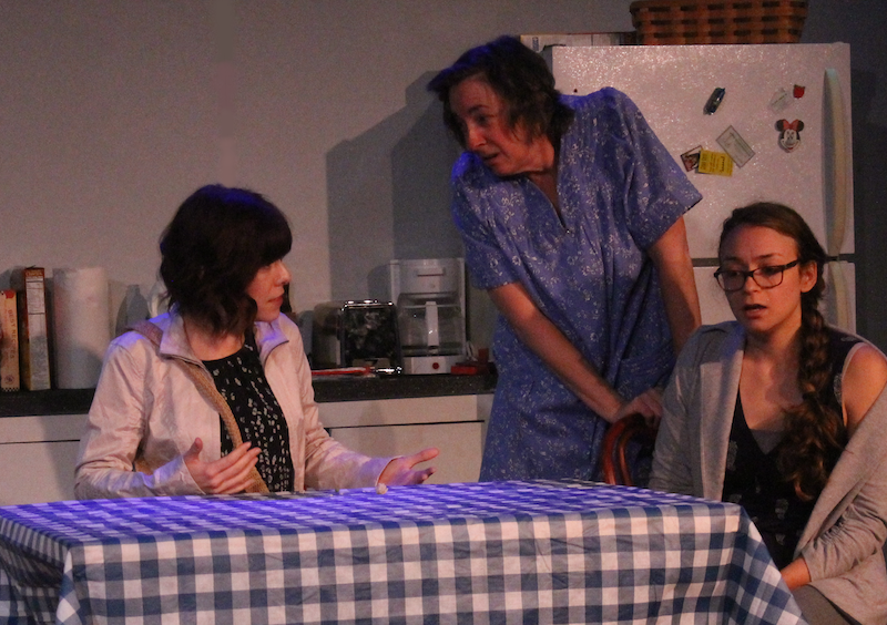 Three actors perform a scene from "Built To Float" around a kitchen table.