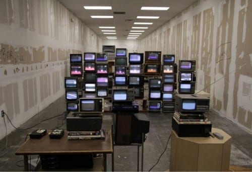 Christopher Chambers; "untitled (Michael)", 2011. 41 TVS (38 functioning), 5 DVD Players, 5 DVDs, 5 RF modulators, 2 VHF broadcast transmitters, coaxial cable, rca cable, coaxial ends, coaxial splitters, found books, donated vhs tapes, coffee table, television stands, external speakers, modified newspaper dispenser, found furniture, speaker wire, extension cords, empty storefront, remote